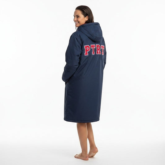 The Swim Guy Online Store navy blue parka with red lining and red "PTRT" lettering with white outline. Model wears it poolside.